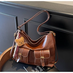 Detail of a brown PU leather tote bag with multi-pockets and a cute plush bear charm