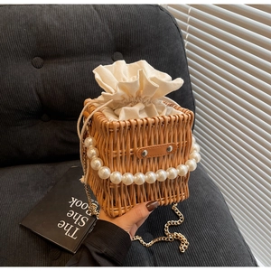 Detailed close-up of woven straw bucket bag with pearl handle and metal chain strap