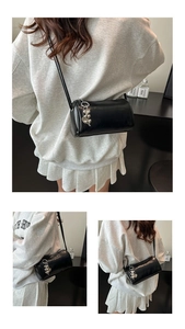 Detail of a black cylinder bag with glossy finish and silver heart pendant decoration