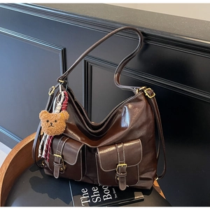 Detail of dark brown tote bag with two front pockets and teddy bear charm on a black chair