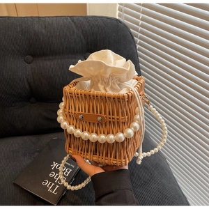 Detail of hand-woven straw bucket bag with elegant pearl strap and inner drawstring pouch