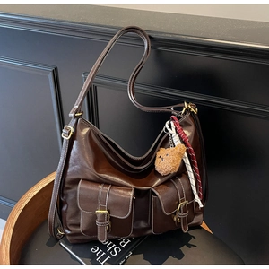 Detail view of large dark brown hobo bag with front buckle pockets and plush charm