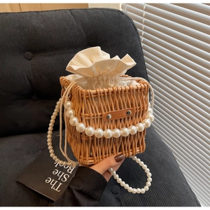 Close-up of hand-woven straw bucket bag featuring elegant pearl chain handle and drawstring lining
