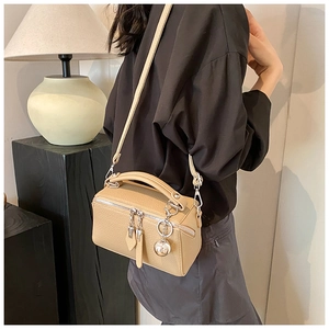 Detail view of a light brown lychee grain Boston bag with dual metal zippers and round charm