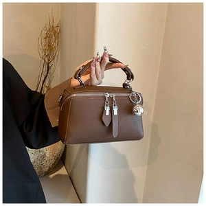 Detail of brown litchi leather bag featuring silver dual zippers and a large metal ball charm
