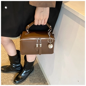 Detail of dark brown leather Boston bag showing textured grain and silver metal ball charm