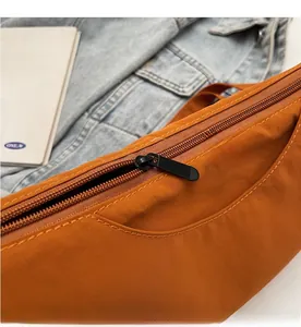 Close-up of smooth black zipper on orange-brown crossbody bag with denim background