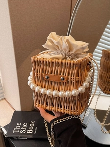 Elegant woven straw bucket bag with pearl handle, gold chain, and drawstring closure