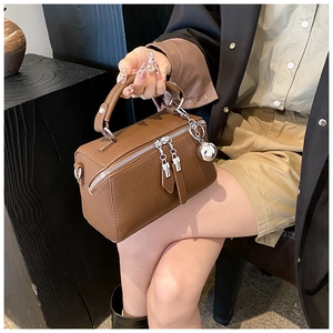 Detailed view of brown lychee leather Boston bag with silver zippers and metal charm