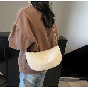 Detailed side view of the cream crescent bag worn across the body with an adjustable strap