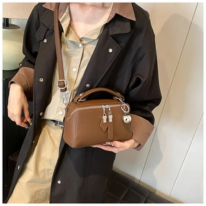 Detail of a brown leather Boston bag with lychee texture and silver ball charm