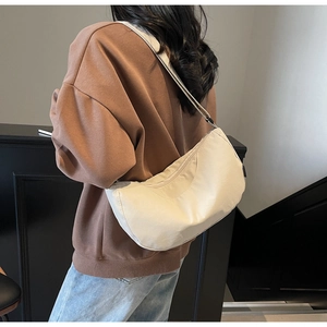 Detail view of a large cream-white crescent nylon crossbody bag on a model side profile