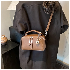 Close-up of brown litchi grain leather bag with dual zippers and metal ball charms