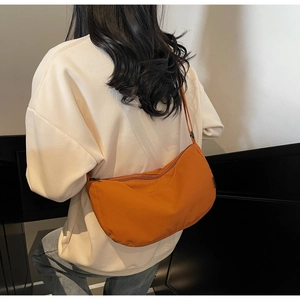 Detail shot of the caramel orange crescent bag worn as a crossbody on a casual outfit