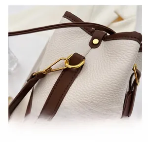 Close-up of golden metal hooks and brown leather strap on a cream bucket bag