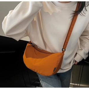 Close-up of orange nylon crescent bag showing adjustable strap and Fashion label detail