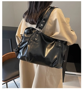 Detail of glossy black tote bag featuring silver metal rivets and moto-style buckle straps