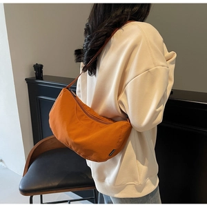 Detailed side view of orange nylon crescent bag with adjustable strap on a model
