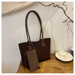 Detail of suede leopard print tote bag with small accessory on a rustic wooden stand