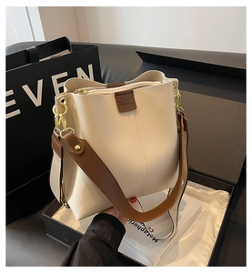 Detailed close-up of cream leather bucket bag with wide strap and gold hardware in luxury setting