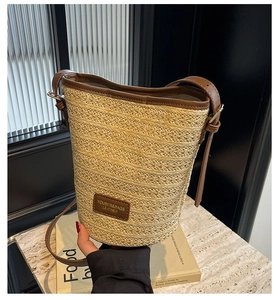 Detailed view of the straw bucket bag with brown leather strap and logo patch