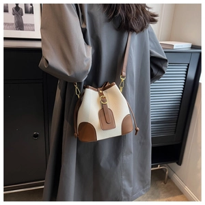 Detail of a cream and brown bucket bag with lychee texture worn over a model's shoulder
