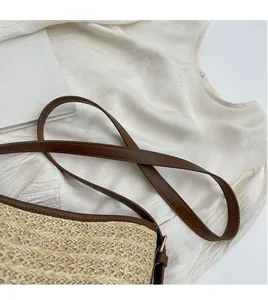 Detail of hand-woven straw bucket bag with adjustable brown leather straps and metal buckle
