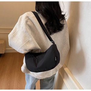 Close-up of black nylon half-moon crossbody bag with adjustable wide strap and fashion tag