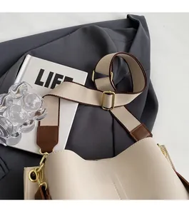 Detail of cream shoulder bucket bag with wide canvas strap and gold metal buckle