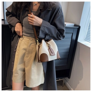 Detail view of a color-blocked bucket bag in white lychee leather with brown accents