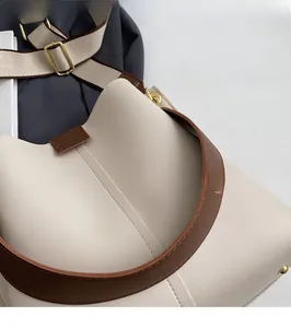 Close-up of beige leather bucket bag featuring brown strap and gold metal studs