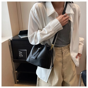 Close-up of black lychee grain leather bucket bag worn as a crossbody by a fashion model