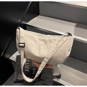 Detailed view of cream nylon crescent bag with adjustable strap on a book base