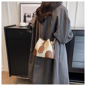 Detail of contrast bucket bag with beige pebbled texture and brown leather strap