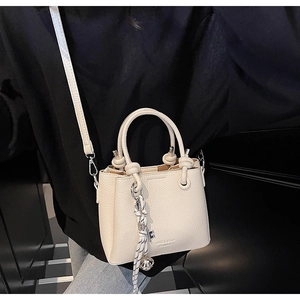 Détail du mini sac seau en cuir grainé crème avec breloque cloche argentée et bandoulière