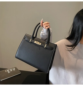 Detail of black pebbled leather handbag with gold metal twist lock and top handles