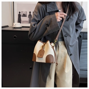 Fashionable crossbody bucket bag in beige and brown leather shown on a model in a room