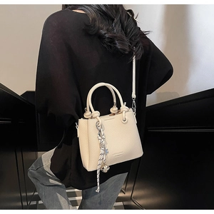 Détail du sac cabas en cuir crème avec breloque tressée et bandoulière sur modèle