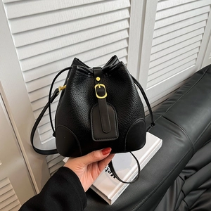 Detail of black lychee grain leather bucket bag featuring gold buckle and drawstring closure