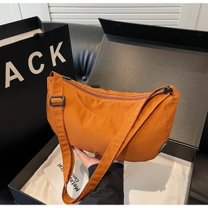 Detail of caramel nylon crescent bag with adjustable strap and fashion label on black background