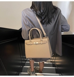 Detailed view of beige luxury handbag with metal twist lock held by a model on stairs