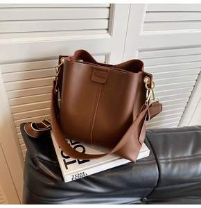 Close-up of brown matte leather bucket bag with golden hardware and adjustable wide strap