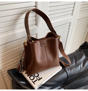 Detail of a brown bucket bag with detachable striped wide strap on a minimalist setup