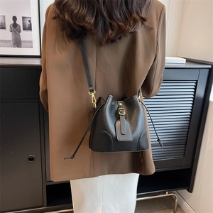 Modern black lychee pattern leather bucket bag with gold hardware on a stylish model