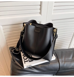 Detailed view of black matte bucket bag with wide strap and gold hardware accents