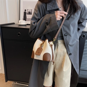 Chic beige and brown crossbody bucket bag styled with a grey coat in a modern setting