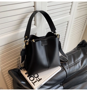 Close-up of black bucket bag with gold metal hardware and textured wide shoulder strap