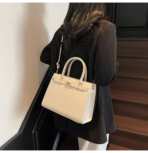 Detail view of cream white top-handle bag with metallic twist lock and adjustable strap