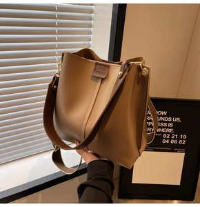 Detail shot of a light brown bucket bag featuring a wide strap and chic leather brand patch