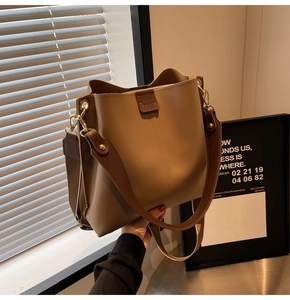 Detail of camel leather bucket bag with vertical stitching and wide brown shoulder strap